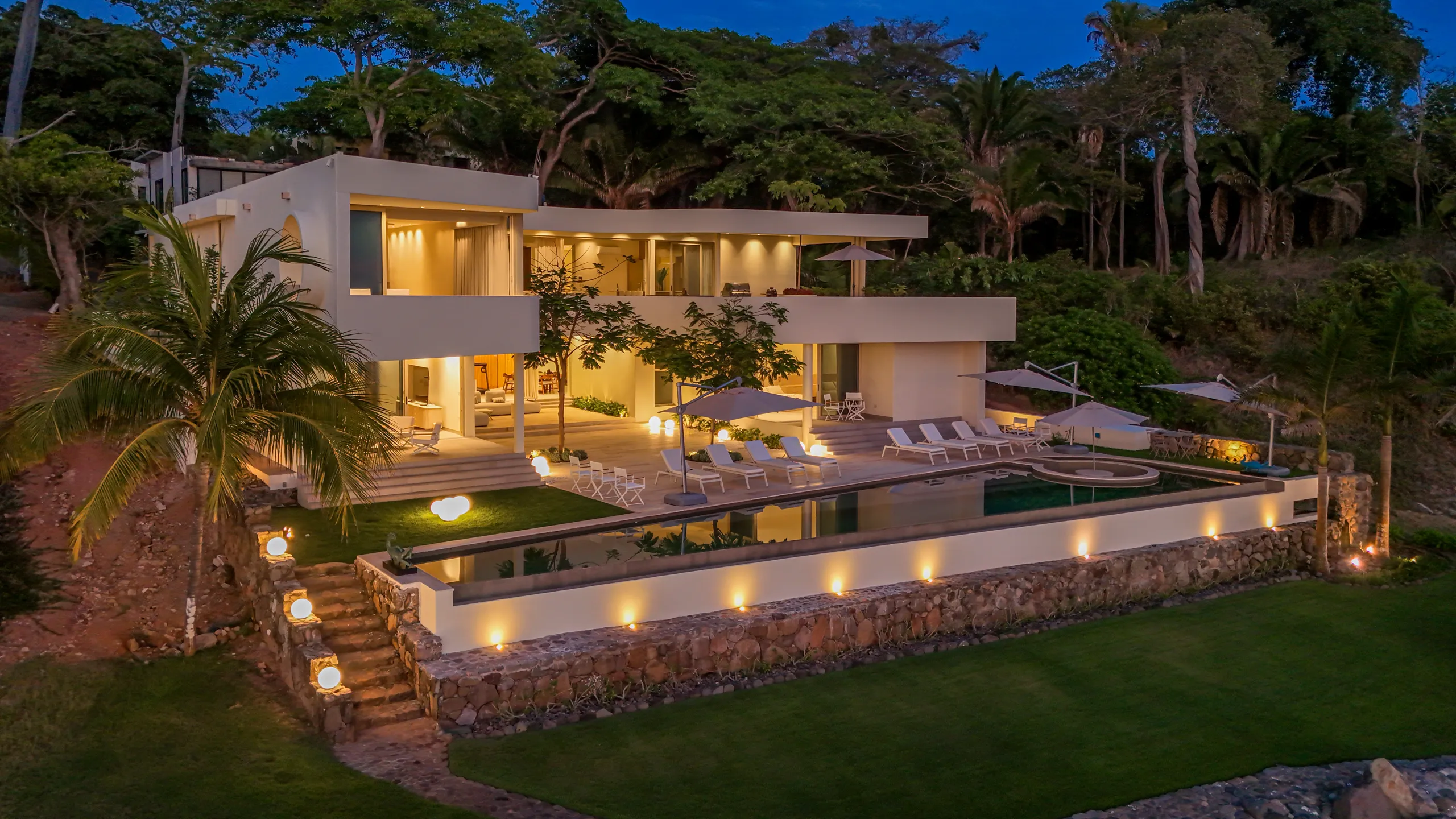 Soft architectural lighting transforms the residence into a refined oceanfront retreat as the coastline transitions into evening.